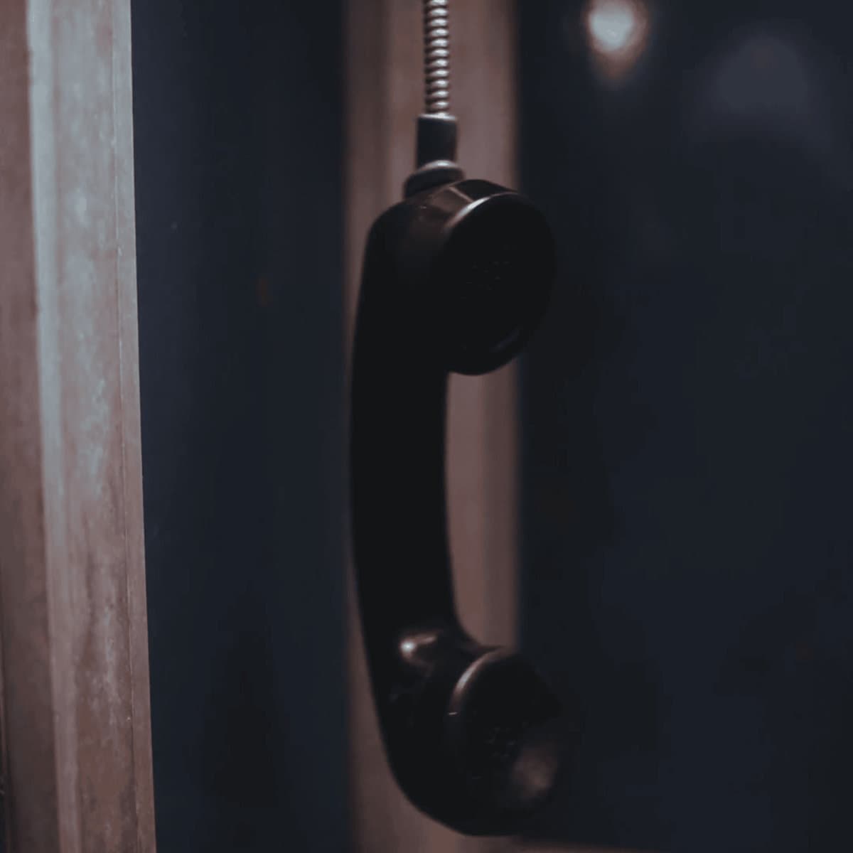 Operator cover: a black payphone handset hanging by its cord in a dim, blue-lit booth